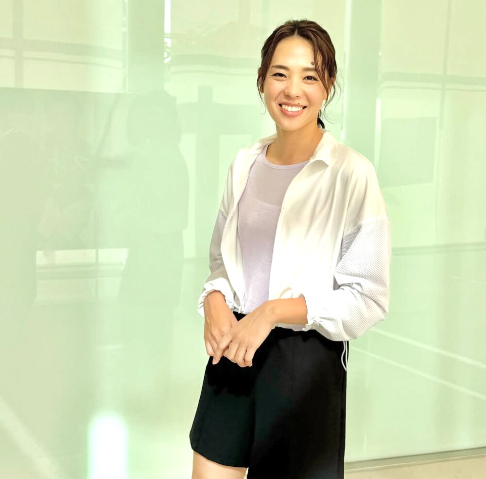 迫田さおりの笑顔の全身写真。白シャツ姿でほくろがチャームポイントの元日本代表選手